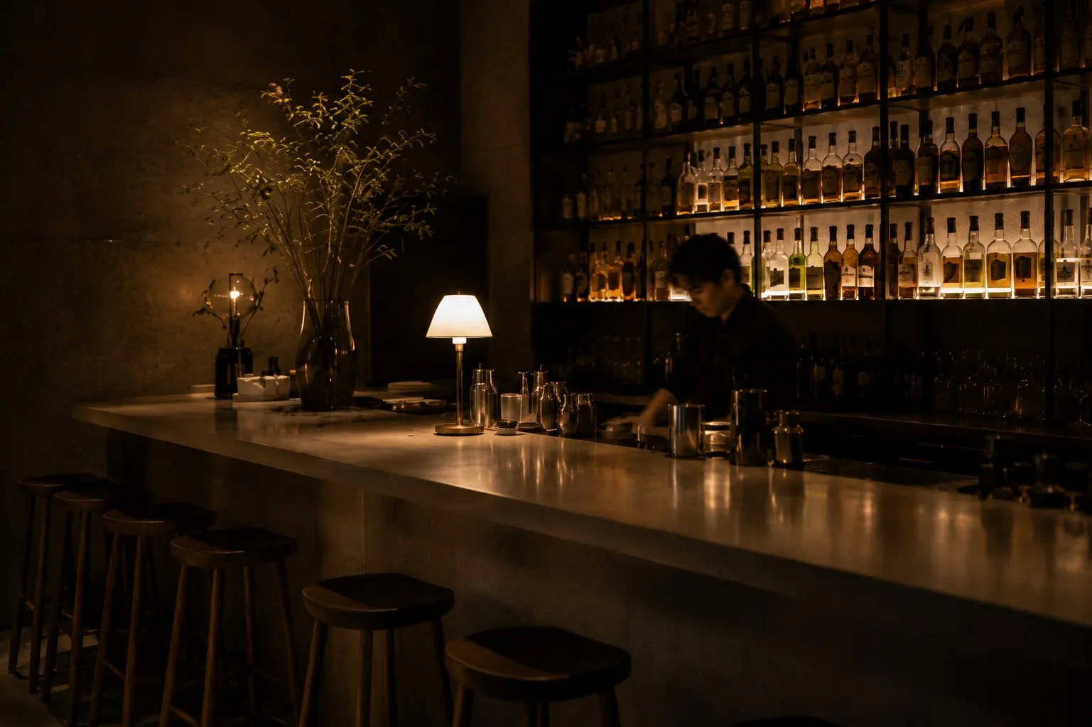 Bar à cocktails feutré, mur de bouteilles, lampe de comptoir.
